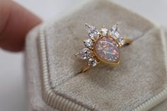 an opal and diamond ring is displayed on a white velvet box with a hand holding it