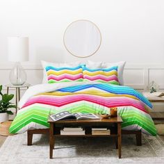 a bed with colorful comforter and pillows in a room next to a coffee table