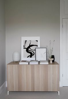 a wooden cabinet with two pictures on top of it next to a white vase and potted plant