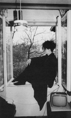 black and white photograph of a woman leaning on a window sill in front of a tv