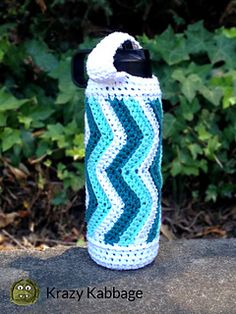 a blue and white crocheted water bottle cover sitting on top of a rock