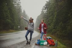 two people standing on the side of a road with luggage and backpacks next to them