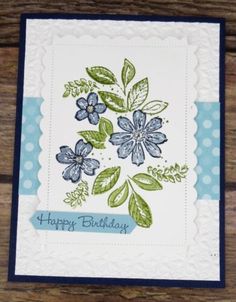 a birthday card with blue flowers and green leaves on the front, sitting on a wooden surface