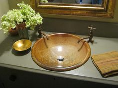 a brown sink sitting on top of a counter next to a vase with flowers in it