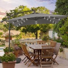 an outdoor dining table and chairs with lights on the umbrella over it in front of a pool