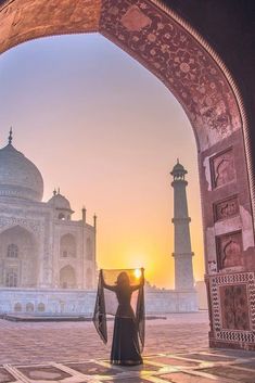 a woman standing in front of an archway with the sun setting behind her and looking into the distance