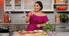 a woman standing in a kitchen holding a knife and fork with food on a cutting board