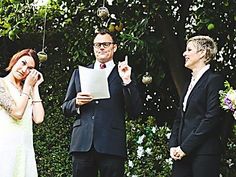 a man and woman standing next to each other in front of a tree holding papers