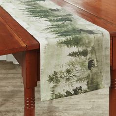 a wooden table with a white and green table runner on it's edge, sitting next to a wood bench