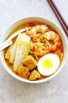 a bowl of soup with shrimp, noodles and egg on the side next to chopsticks