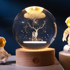 two small figurines are next to a snow globe with an image of a deer