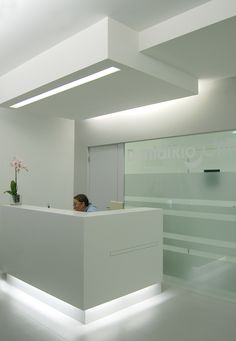 a man sitting at a desk in an office with white walls and ceiling lights on either side