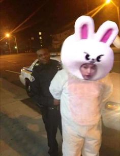 a man in bunny suit standing next to a police officer on the street at night