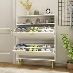 a white shoe rack filled with shoes next to a potted plant