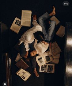 two people laying on the floor surrounded by books and papers, looking down at them