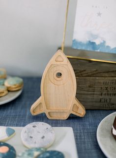 a wooden toy rocket ship sitting on top of a table next to plates and cookies