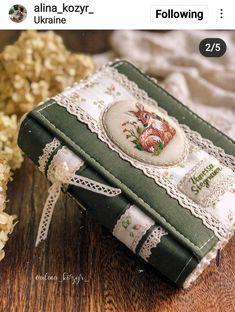 an old book is decorated with flowers and lace on the cover, sitting on a wooden table