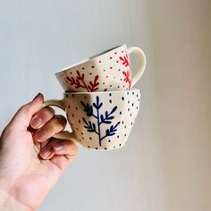 someone holding two cups in their hand with red, white and blue designs on them