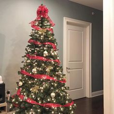 a decorated christmas tree with red bows and lights in a room next to a door