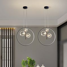 two circular lights hanging from the ceiling above a dining room table with chairs and potted plant