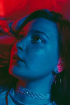 a woman with large hoop earrings on her neck looking up at something red and blue