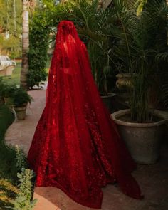 a woman wearing a red cape standing in front of some potted plants and greenery