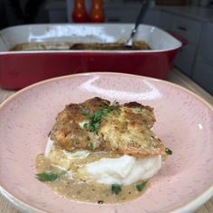 a pink plate topped with mashed potatoes covered in gravy next to a casserole dish