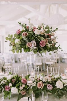 a tall vase filled with pink and white flowers on top of a table covered in greenery