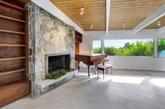 an empty living room with stone fireplace and wood paneled ceiling, along with large windows