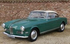 an old green car parked in front of a brick wall