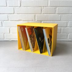 a yellow book holder with four books in it and a brick wall behind the shelf