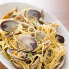 pasta with clams and sauce in a white bowl on a wooden table top, ready to be eaten