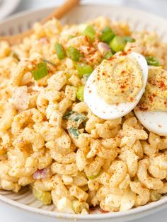 a white bowl filled with macaroni salad and an egg on top, sitting on a table