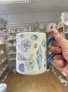 a hand holding a coffee mug in a store filled with shelves and other items on display