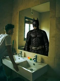 a man standing in front of a bathroom mirror next to a sink with a batman image on it