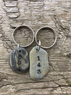 two stone keychains with numbers on them sitting on a piece of drift wood