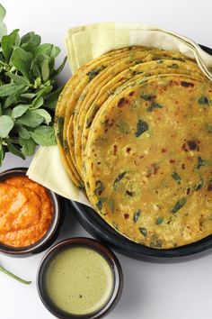 a plate filled with tortillas next to some dipping sauces and green leaves