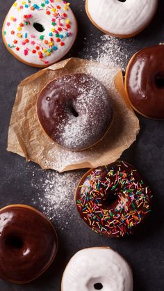 six donuts with chocolate frosting and sprinkles sitting on wax paper