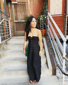 a woman is standing on the steps in front of some stairs and holding a green purse