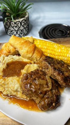 a white plate topped with meat, potatoes and gravy next to a corn on the cob