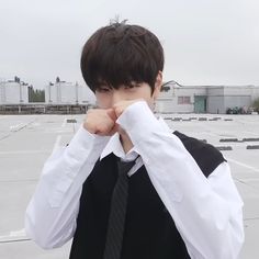 a young man wearing a white shirt and black tie with his hands on his face