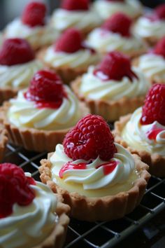 small desserts with white frosting and raspberries are on a cooling rack