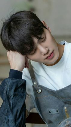 a young man sitting on top of a wooden chair holding his hand to his head