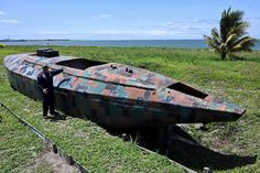 a man standing next to an old boat on the grass