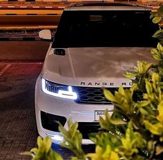 a white range rover is parked in front of some bushes