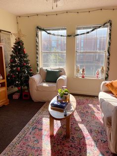 a living room filled with furniture and a christmas tree in front of two large windows