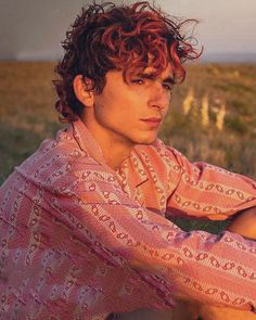 a young man with red hair sitting in a field