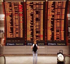 a woman standing in front of an airport departure board