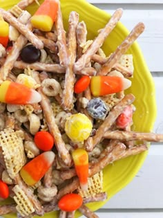 a yellow plate topped with candy corn and pretzel snack mix on top of a white wooden table