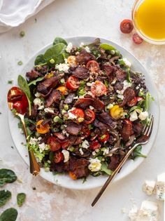 a white plate topped with salad next to a glass of orange juice and two spoons